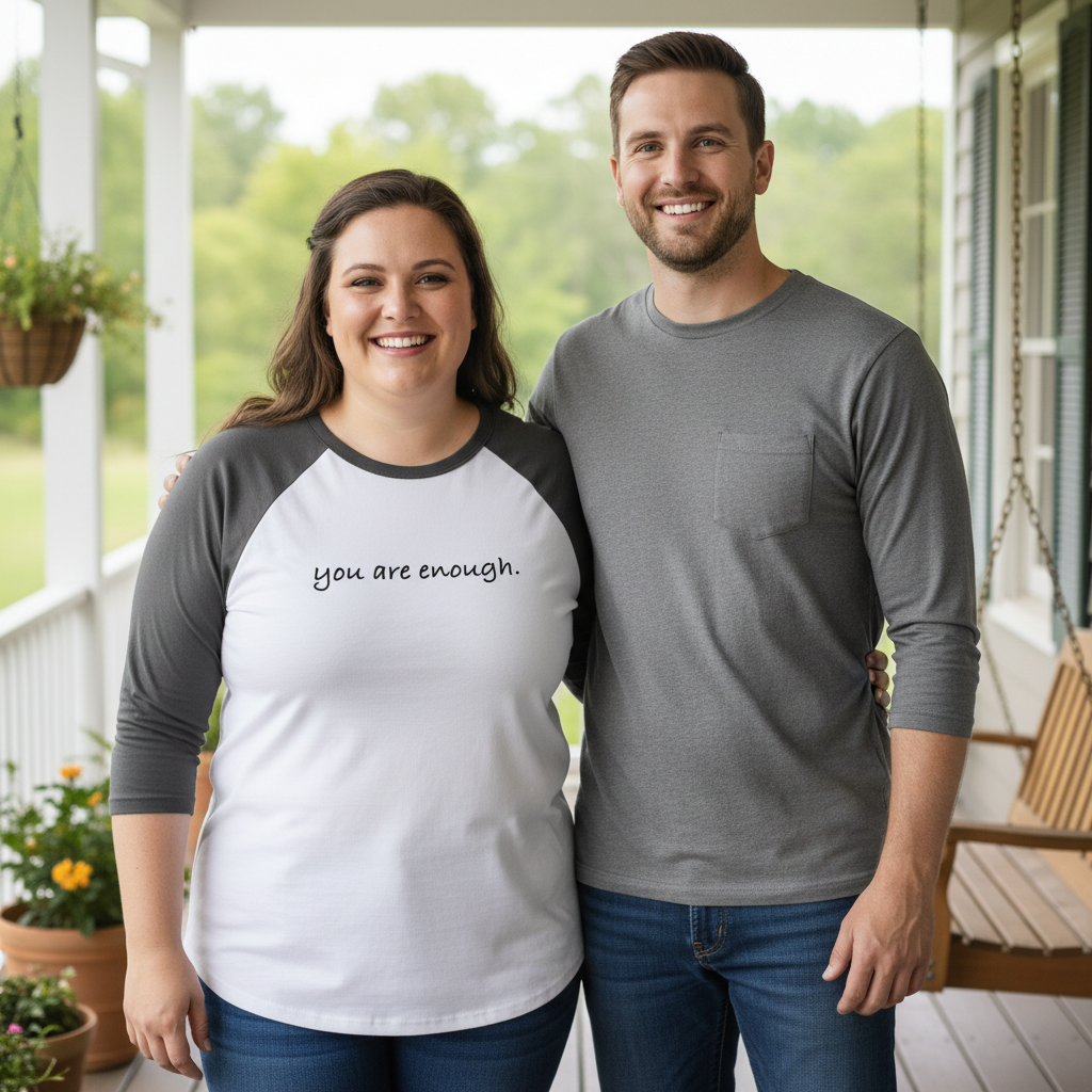 Smiling couple standing together on a porch, with the woman wearing a white and gray raglan shirt that says "you are enough." A heartwarming lifestyle photo promoting positivity, love, and self-acceptance through minimalist fashion.